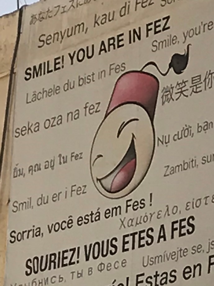 A sign with the words, "Smile! you are in Fez" in multiple languages.